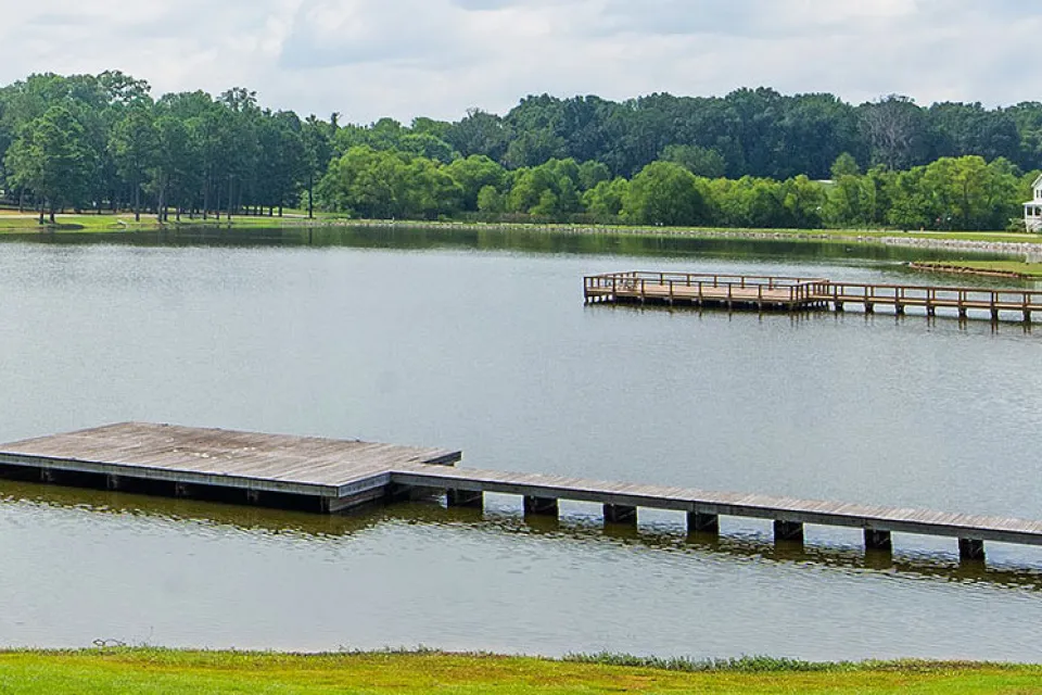View of docks on lake surrounded by green trees and lawns with one white house at right